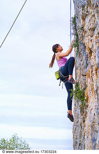 Vertical profile photo of a young woman rock climbing outdoors