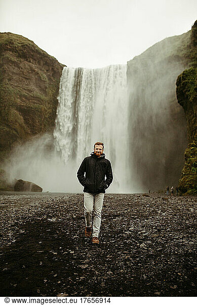 Vertical Shot of a Man in Front of a Waterfall