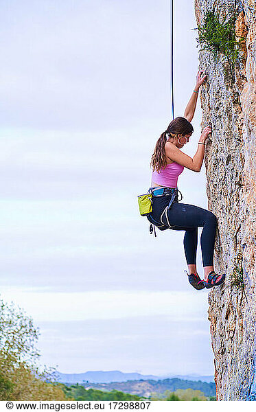 Vertikales Profilfoto einer jungen Frau  die eine steile Felswand erklimmt