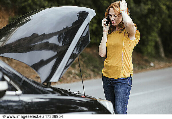 Verwirrte Frau kratzt sich am Kopf  während sie im Auto mit dem Handy telefoniert