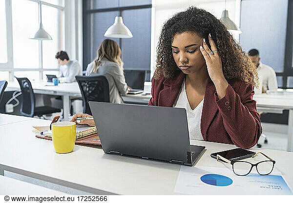 Verwirrte weibliche Fachkraft bei der Arbeit mit männlichen und weiblichen Kollegen im Hintergrund im Büro