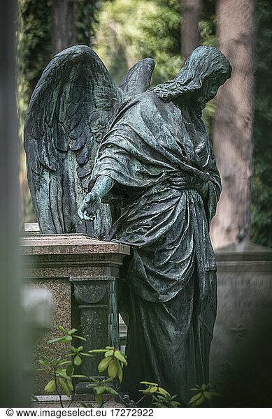 Verwitterte Statue eines Engels neben einem Grab auf dem Friedhof