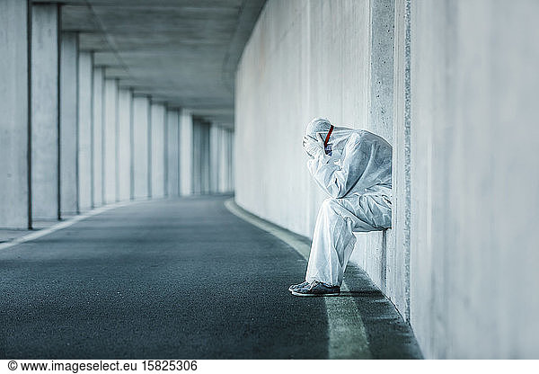 Verzweifelter Mann in Schutzkleidung sitzt in einer Nische einer Betonwand in einem Tunnel