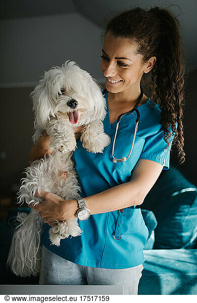 Veterinarian holding and petting a fluffy white dog and smiling.
