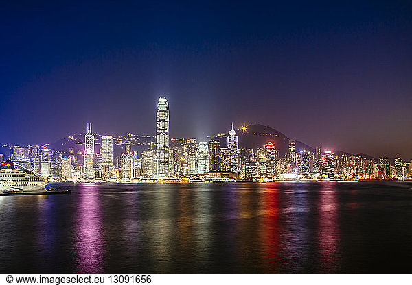 Victoria harbour against illuminated Two International Finance Center and buildings in city at night