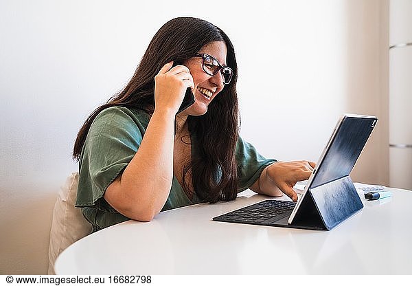 Video of a young spanish brunette girl talking with the phone and teleworking with her hybrid tablet laptop adapting her business to the new normal after the covid 19 global pandemic.