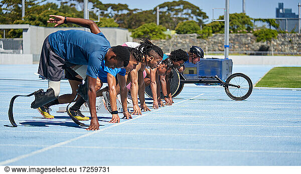 Vielfältige Athleten stehen an der Startlinie auf der sonnigen blauen Sportbahn bereit