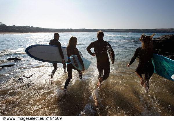 Vier Leute laufen mit Surfbrettern ins Wasser.
