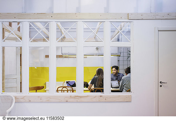 Vier Personen diskutieren in einer Besprechung durch ein Glasfenster im Büro.