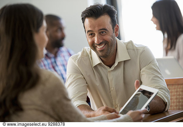 Vier Personen in einem Büro  zwei Männer und zwei Frauen. Zwei schauen auf einen digitalen Tablet-Bildschirm.