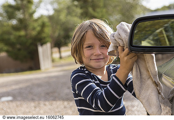 Vierjähriger Junge  der ein Auto außen mit Reiniger und einem Tuch poliert