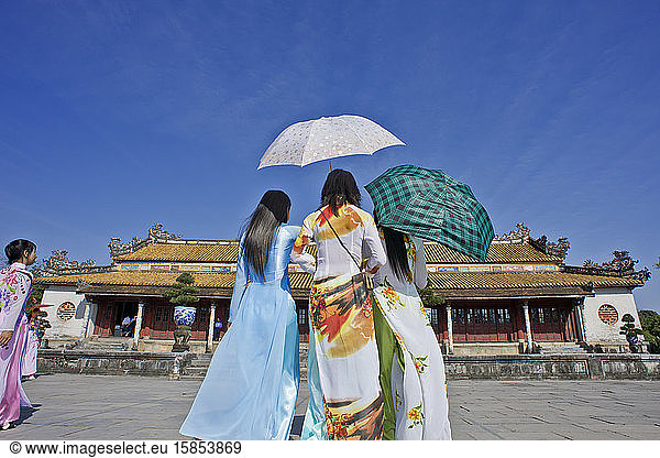 Vietnamesische Touristen in Kleidern Ao dai mit Regenschirmen in der Zitadelle