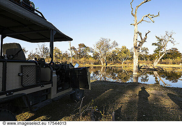 View across flat calm water from a jeep by a waterway  in a wildlife reserve.