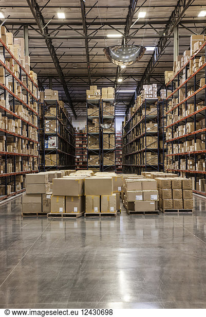 View down aisles of racks holding cardboard boxes of product on pallets in a large distribution warehouse