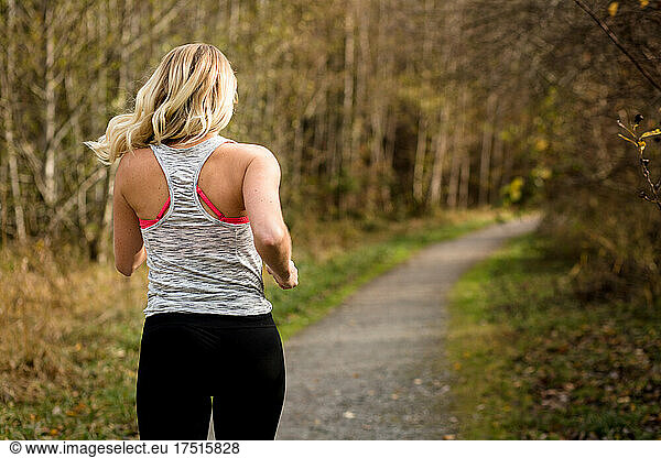 View from behind of blonde woman running on wooded trail