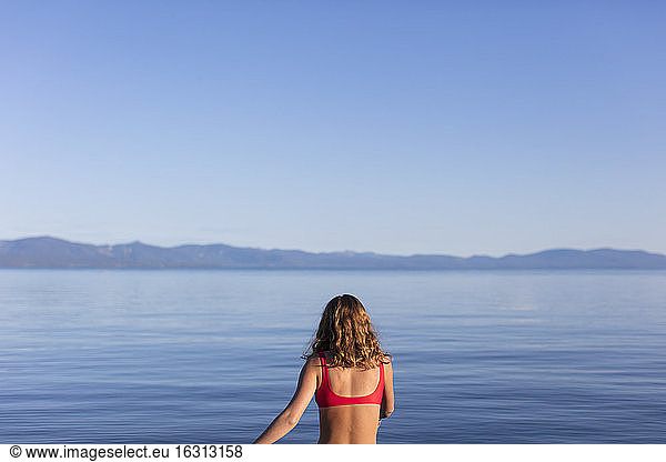 View from behind of woman entering calm  blue waters of a lake at dawn