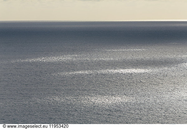 View from the land over the ocean  to the horizon in low light. Sunlight patches on the water surface.
