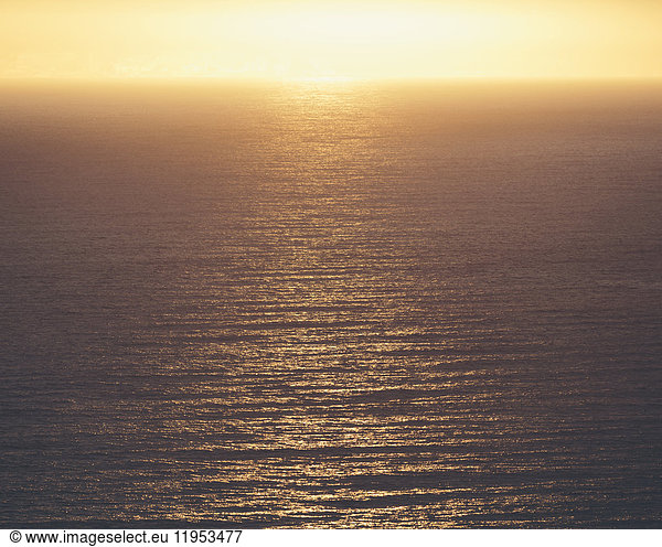 View from the land over the ocean  to the horizon. The sun resting on the horizon and light reflecting off the water.