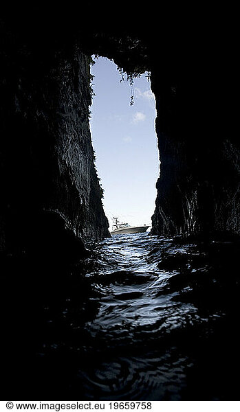 View of a boat floating in the water  through the narrow opening of a dark cave in Costa Rica.