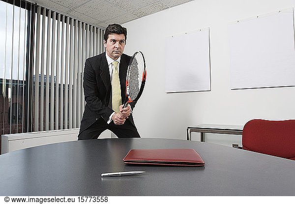 View of a business man holding a tennis racquet in an office.