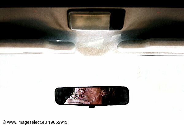 View of a man smoking a cigarette in a rear view mirror
