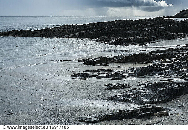 View of a sandy beach and rocky shore under a cloudy sky.