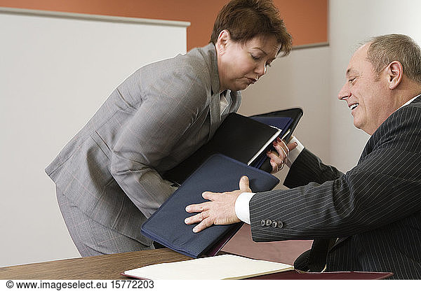 View of business man helping business woman hold files.