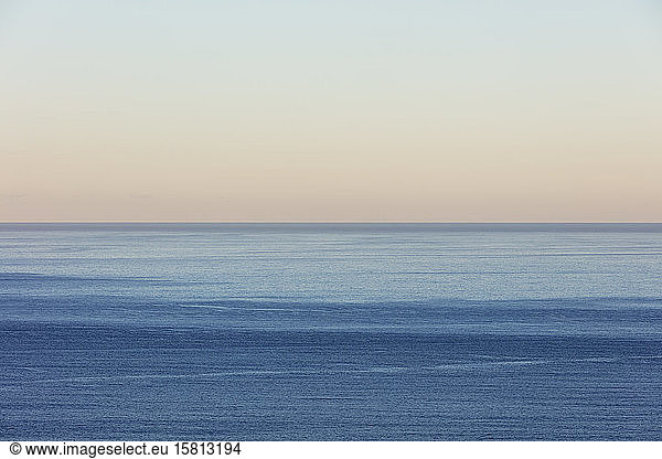 View of calm ocean waters  horizon and sky at dawn