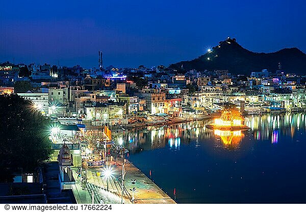 View of famous indian hinduism pilgrimage town sacred holy hindu religious city Pushkar with Brahma temple  aarti ceremony  lake and ghats illuminated at sunset. Rajasthan  India. Horizontal pan