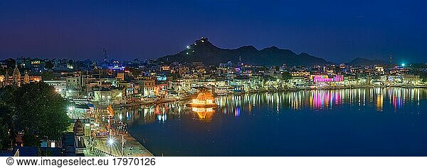 View of famous indian hinduism pilgrimage town sacred holy hindu religious city Pushkar with Brahma temple  aarti ceremony  lake and ghats illuminated at sunset. Rajasthan  India. Horizontal pan