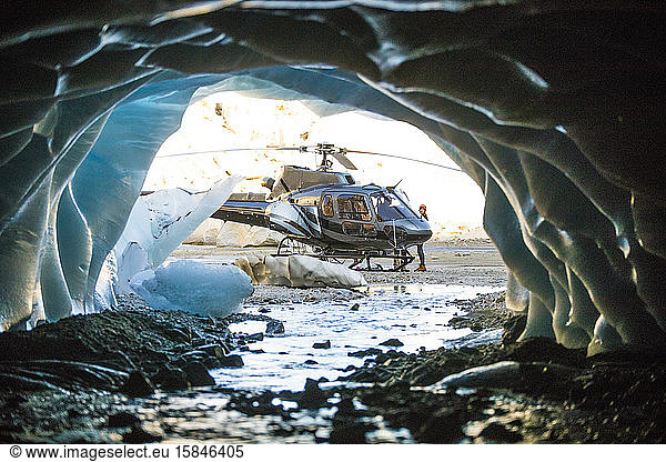 View of helicopter landed outside of a glacial cave.