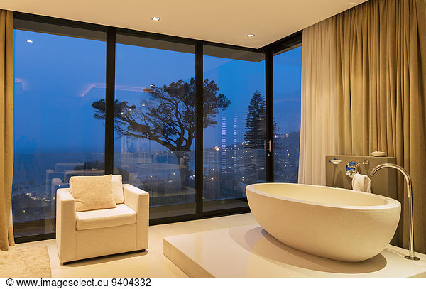 View of luxurious bathroom with bathtub and armchair at night