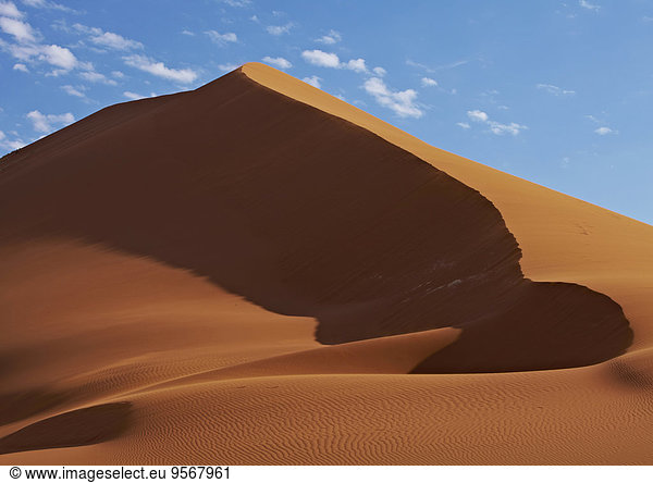 View of sand dunes in desert with blue sky and clouds in background