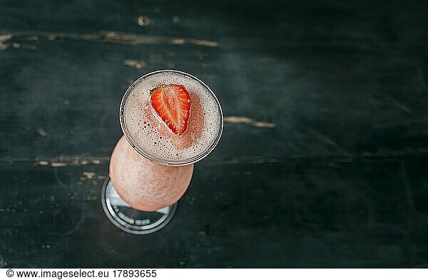 View of strawberry milkshake on dark wood. View from above of delicious strawberry smoothie with a strawberry on top on wood. Top view of strawberry smoothie on dark wooden table