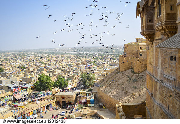 View of the city of Jaisalmer from the historic hilltop fort with large birds in the air above the market.