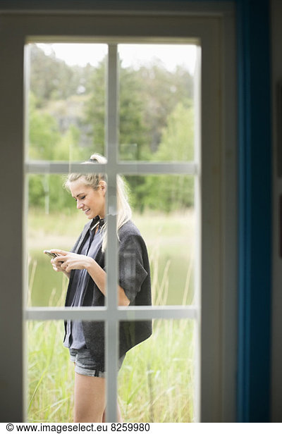 View of woman using mobile phone through closed door
