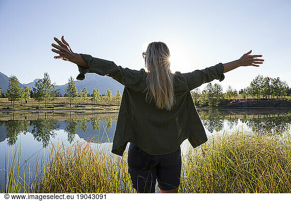 View past woman greeting sunrise over mountain pond