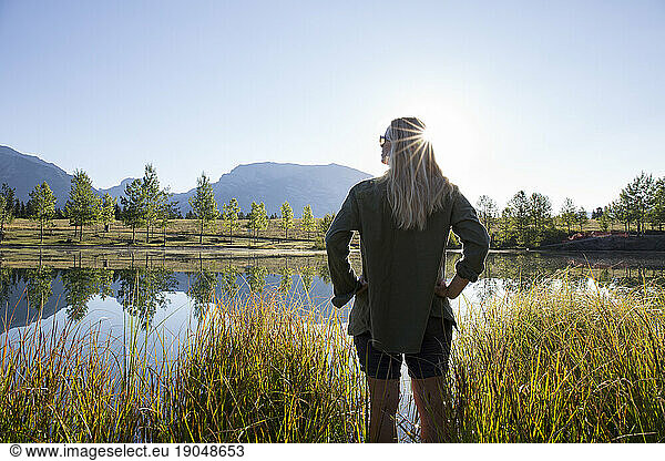 View past woman greeting sunrise over mountain pond