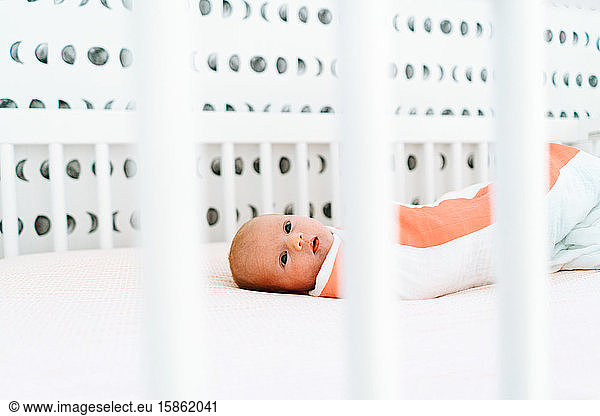 View through a crib of a newborn baby girl laying down