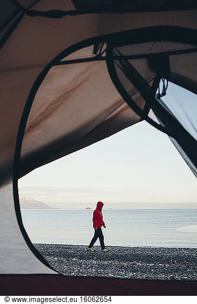 View through doorway of camping tent of woman walking on beach Muir Inlet in distance Glacier Bay National Park Alaska