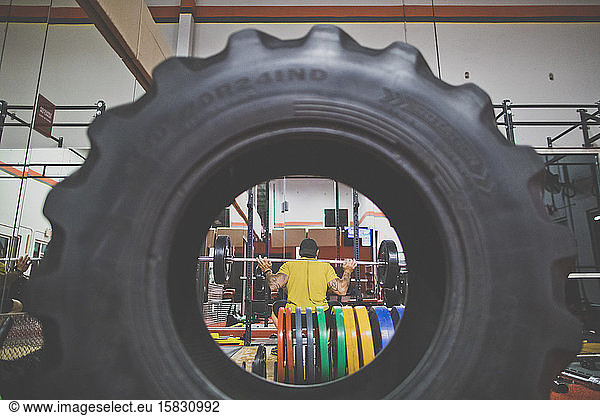 View through tire of bodybuilder doing squats at the gym