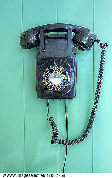 Vintage rotary landline phone hanging on turquoise wooden wall at barber shop