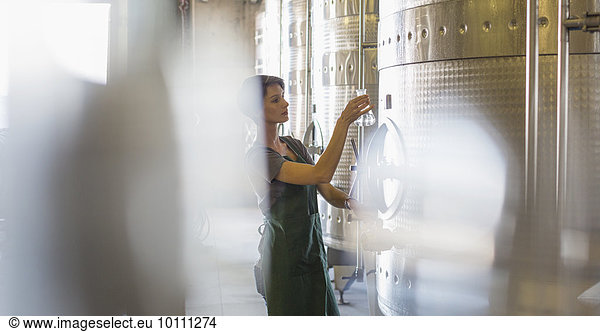Vintner testing wine from stainless steel vat in winery cellar