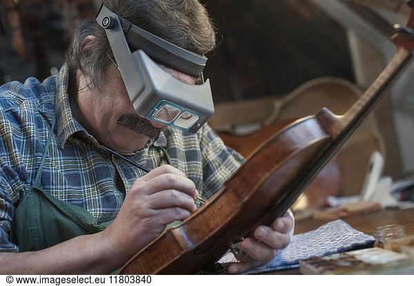 Violin maker painting violin using magnification