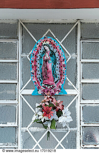 Virgin Mary figurine with flowers on metal grate