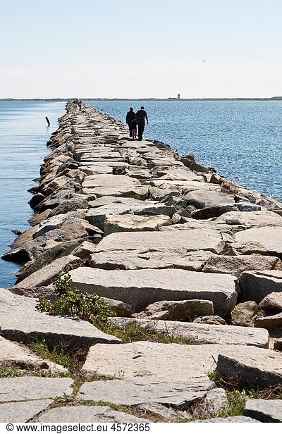Visitors walk across west end of Provincetown Harbor on stone walkway from Provincetown to outlying beach on the tip of Cape Cod