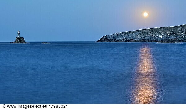 Vollmond  Mond über Felsenküste  Strahl des Mondlichts auf dem Meer  Meer ruhig  Himmel blau und wolkenlos  Leuchtturm auf winziger Felseninsel leuchtet  Insel Andros  Kykladen  Griechenland  Europa