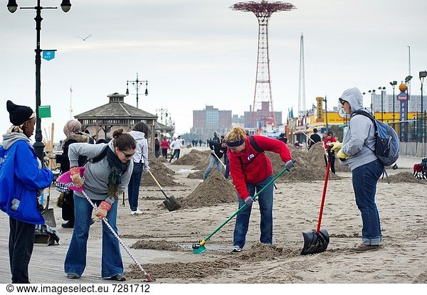 Volunteers armed with gloves  shovels and brooms clean up debris and sand deposited by Hurricane Sandy from the beach and boardwalk of the Brighton and Coney Island beach neighborhoods of New York The destructive Hurricane pushed tons of sand inland with. Volunteers armed with gloves  shovels and brooms clean up debris and sand deposited by Hurricane Sandy from the beach and boardwalk of the Brighton and Coney Island beach neighborhoods of New York The destructive Hurricane pushed tons of sand inland with its storm surge as well as carrying destroyed property onto the beach  some of it from the devastated Rockaway Peninsula Hundreds of volunteers organized by the NYC Mayor´s office performed a day of service helping people in Brooklyn  Staten Island and Rockaway