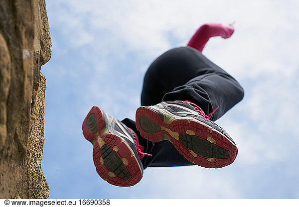 Von unten springt eine Frau in Turnschuhen von einer rauen Steinmauer