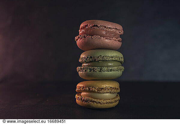 Vorderansicht von drei Macarons in verschiedenen Farben auf dunklem Hintergrund